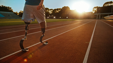 Athletic Disabled Fit Man with Prosthetic Running Blades is Walking During a Training on an Outdoor Stadium on a Sunny Afternoon. Amputee Runner Preparing for a Run. Motivational Sports Shot. - obrazy, fototapety, plakaty
