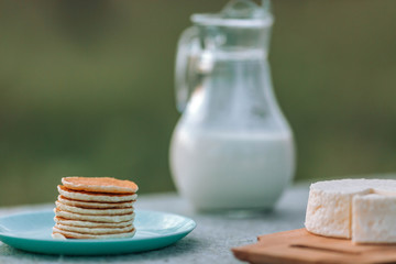 Pancake cheese with a jug and a glass of milk for breakfast on the table, in a rustic style.