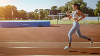 Beautiful Fitness Woman in Light Blue Athletic Top and Leggings Jogging in the Stadium. She is Running Fast on a Warm Summer Afternoon. Athlete Doing Her Routine Sports Practice.