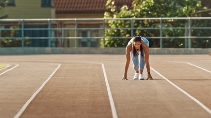 Fototapeta premium Beautiful Fitness Woman in Light Blue Athletic Top and Leggings is Starting a Sprint Run in an Outdoor Stadium. She is Running on a Warm Summer Day. Athlete Doing Her Sports Practice.