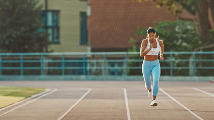 Fototapeta na wymiar Beautiful Fitness Woman in Light Blue Athletic Top and Leggings is Starting a Sprint Run in an Outdoor Stadium. She is Running on a Warm Summer Day. Athlete Doing Her Sports Practice.