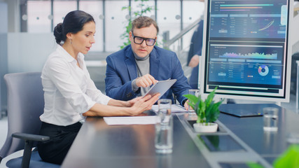 In the Meeting Room Female Executive Shows Digital Tablet Computer to Creative Venture Capitalist, They Discuss Statistics and Investment Capital. Busy Corporate Office with Businesspeople Working