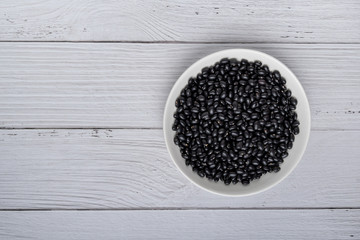 Black beans in white bowl on white wood background. top view. vegan food concept