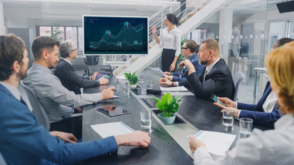 In the Corporate Meeting Room: Female Analyst Uses Digital Interactive Whiteboard for Presentation to a Board of Executives, Lawyers, Investors. Screen Shows Company Growth Data with Graphs
