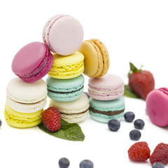 Multicolored macaroons on a white background with strawberries, raspberries, mint and blueberries