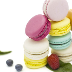 Multicolored macaroons on a white background with strawberries, raspberries, mint and blueberries