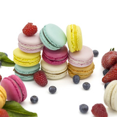 Multicolored macaroons on a white background with strawberries, raspberries, mint and blueberries