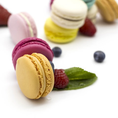 Multicolored macaroons on a white background with strawberries, raspberries, mint and blueberries