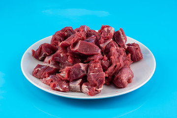 chopped small pieces of raw beef meat, tenderloin on a white plate on a blue background