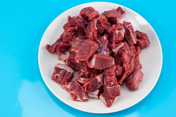 chopped small pieces of raw beef meat, tenderloin on a white plate on a blue background