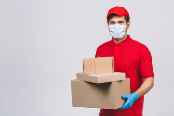 Delivery man employee in red cap blank t-shirt uniform face mask gloves hold empty cardboard box isolated on white background. Service quarantine pandemic coronavirus virus 2019-ncov concept.