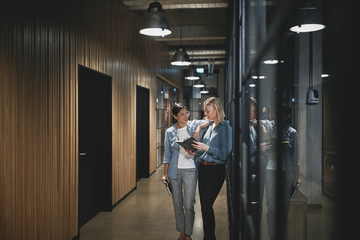 Two businesswomen talking together in an office hallway