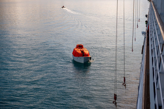 Maneuvering orange lifeboat in water in Arctic waters, Svalbard. Abandon ship drill. Lifeboat training. Man over board drill.
