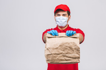 Delivery man employee in red cap blank t-shirt uniform face mask gloves hold empty cardboard box isolated on white background. Service quarantine pandemic coronavirus virus 2019-ncov concept.