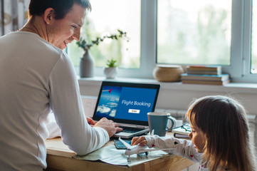 Father booking flights working on the notebook near daughter playing with airplane toy