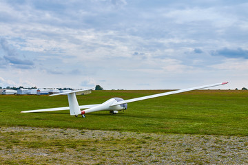 Fototapeta na wymiar Glider plane standing on grass airport runway with dramatic sky background.