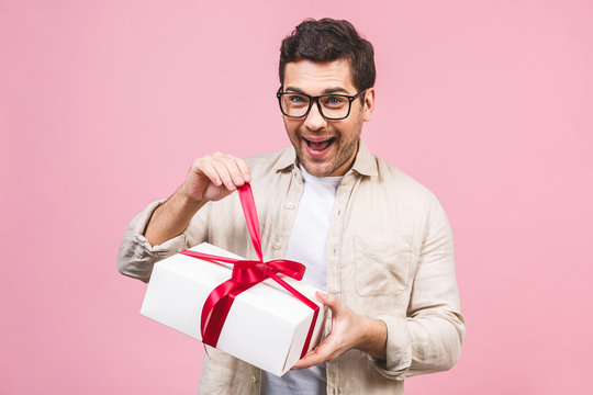 Holiday Concept. Portrait Of A Young Man Opening Gift Box Isolated Over Pink Background.