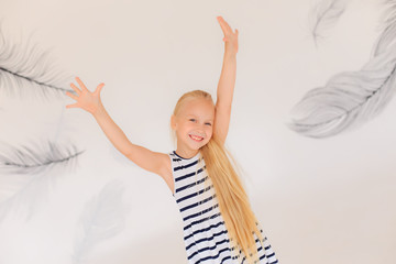 Beautiful girl in a striped dress on a white background. Smiling girl dancing and spinning. Hands up. Blurred background