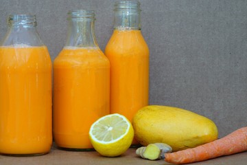Glass bottles filled with colorful fresh homemade mango, carrot and ginger smoothies
