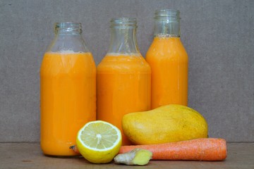 Glass bottles filled with colorful fresh homemade mango, carrot and ginger smoothies