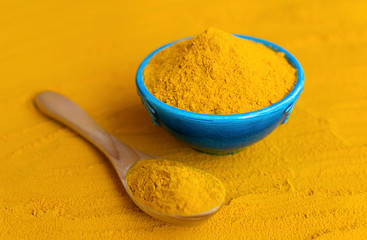 Turmeric powder in blue bowl with wooden spoon at orange background.