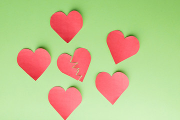 Fototapeta na wymiar Five paper hearts surrounding one '' broken, lonely, down '' Green background.