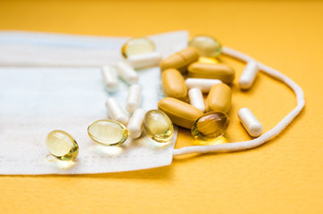Antibiotics and pills of white and yellow lay on medical mask. Paper textured background and white textile mask