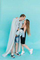 A handsome prince and gorgeous princess in love with a toy horse and plaid cloak are isolated on a blue background. The concept of beauty, romance.