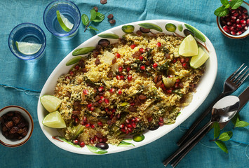 couscous is cooked on orange juice with boiled vegetables, caramelized onions, raisins and pomegranate seeds. on the table with a linen tablecloth