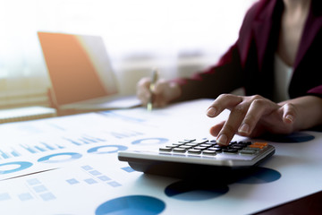 Business Woman or accountant using calculator for calculation and writing to notebook with finance report, tax document, profit loss account on table business office workplace. Business concept.