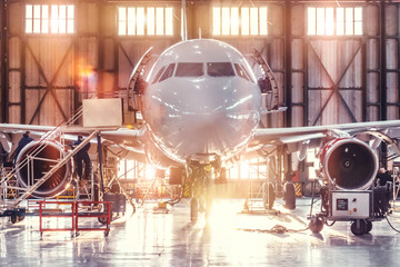 Airplane under repair in the aerospace hangar in the background of the gate and bright sunlight.