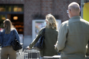Menschen mit Maske stehen mit einem Einkaufswagen geduldig in einer Warteschlange