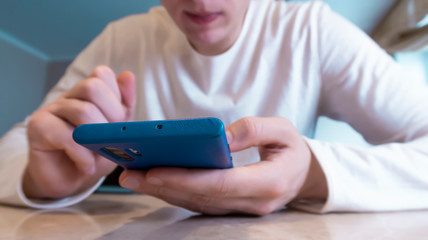 Front view close up of a young Caucasian man sitting at a table using a smartphone at home