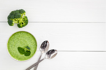 Broccoli vegan cream soup in bowl on white wooden table from above copy space