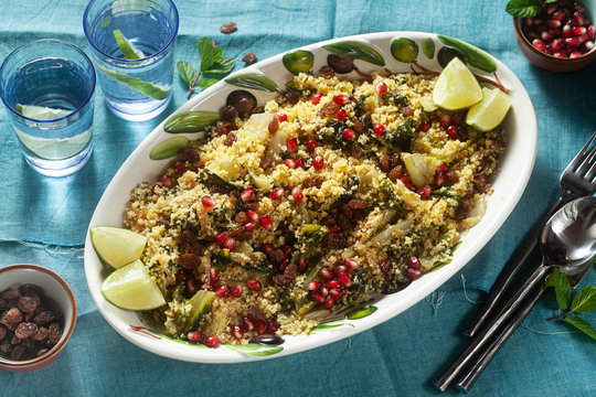 couscous is cooked on orange juice with boiled vegetables, caramelized onions, raisins and pomegranate seeds. on the table with a linen tablecloth