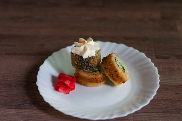 Fried sushi on a white plate with greens, cream cheese and ginger on wooden background front view