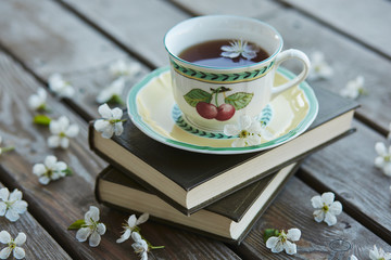 A cup of tea on a pile of books covered with cherry flowers