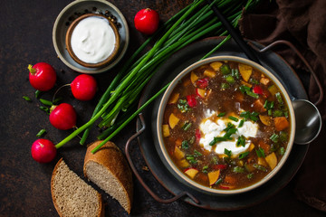 Traditional dish Russian cuisine. Cold summer Okroshka soup with kvass, sausage and vegetables in a bowl on a dark stone countertop. Top view flat lay background.
