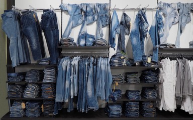 Large assortment of jeans denim trousers and shirts hanging or arranged on the shelf of a clothing store