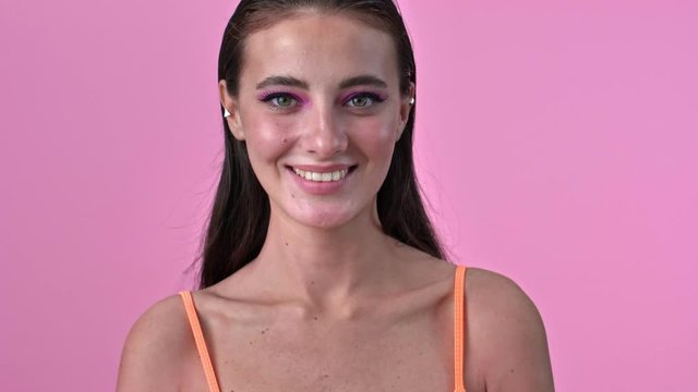 Young cute positive woman isolated over pink wall posing background winking raise her brow