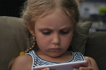 Portrait of a concentrated little girl using mobile phone while sitting on couch 