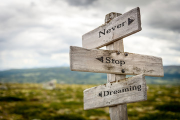 never stop dreaming text engraved on old wooden signpost outdoors in nature. Quotes, words and...