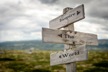 inspire the world text engraved on old wooden signpost outdoors in nature. Quotes, words and illustration concept.