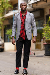 Full body shot of young bald African businessman with scarf outdoors