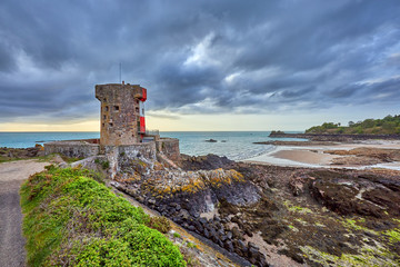 Fototapeta na wymiar Image of Archirondel bay with a Napoleonic Jersey Tower with cloudy morning sky and low tide. Jersey Channel Islands