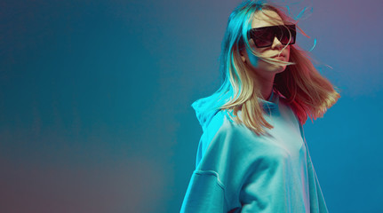 Portrait of a stylish young girl, cool posing in a hoodie, sunglasses and with developing hair, on...