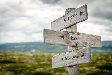 stop the madness text engraved on old wooden signpost outdoors in nature. Quotes, words and illustration concept. - obrazy, fototapety, plakaty