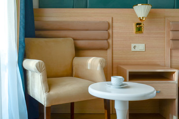 White tea cup and saucer on a round white table against a beige chair