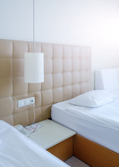 Sunny room in a hotel in light colors with two beds, bedside table and a lamp