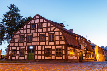Buildings in night city with lantern. Lithuanian town. Center of Klaipeda. Night life. Empty street with lighted buildings. Walking through the street. Deep blue sky and historical house.  Twilight.
